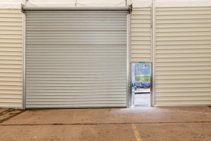 Innenansicht einer Industriehalle mit geschlossenem Rolltor und geöffneter Fluchttür