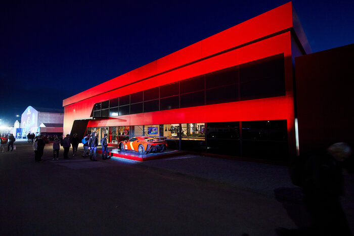 Seitliche Nachtaufnahme Skyline-Eventzelts mit roter Fassade und Sportwagen bei Nacht