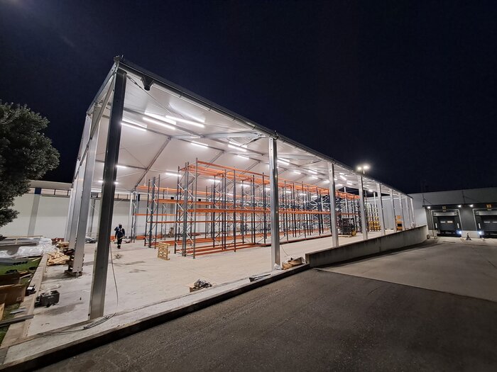 Industriehalle als Logistikzentrum bei Nacht mit beleuchtetem Dach und aufgebauten Hochregalen