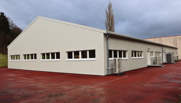 Exterior view of a modular industrial building with aluminium frames and white wall panels on red flooring