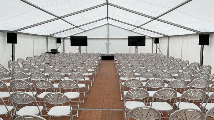 Innenansicht eines Veranstaltungszelts mit Stuhlreihen und Bildschirmen