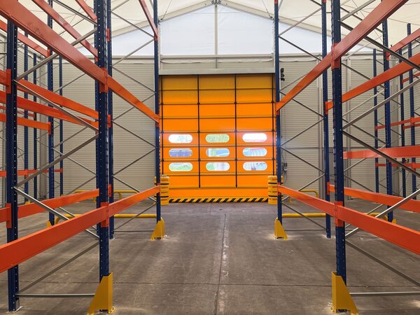 Interior view of a warehouse with an open yellow sectional door and empty floor