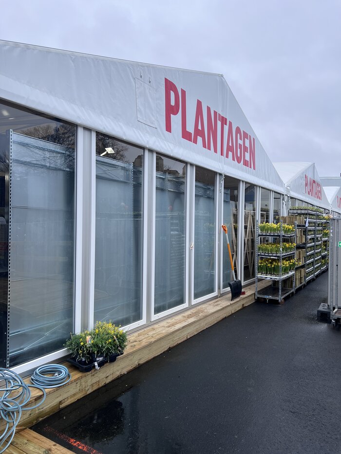 Seitliche Außenansicht eines Eventzelts mit großen Glasfenstern und Verkaufsregalen