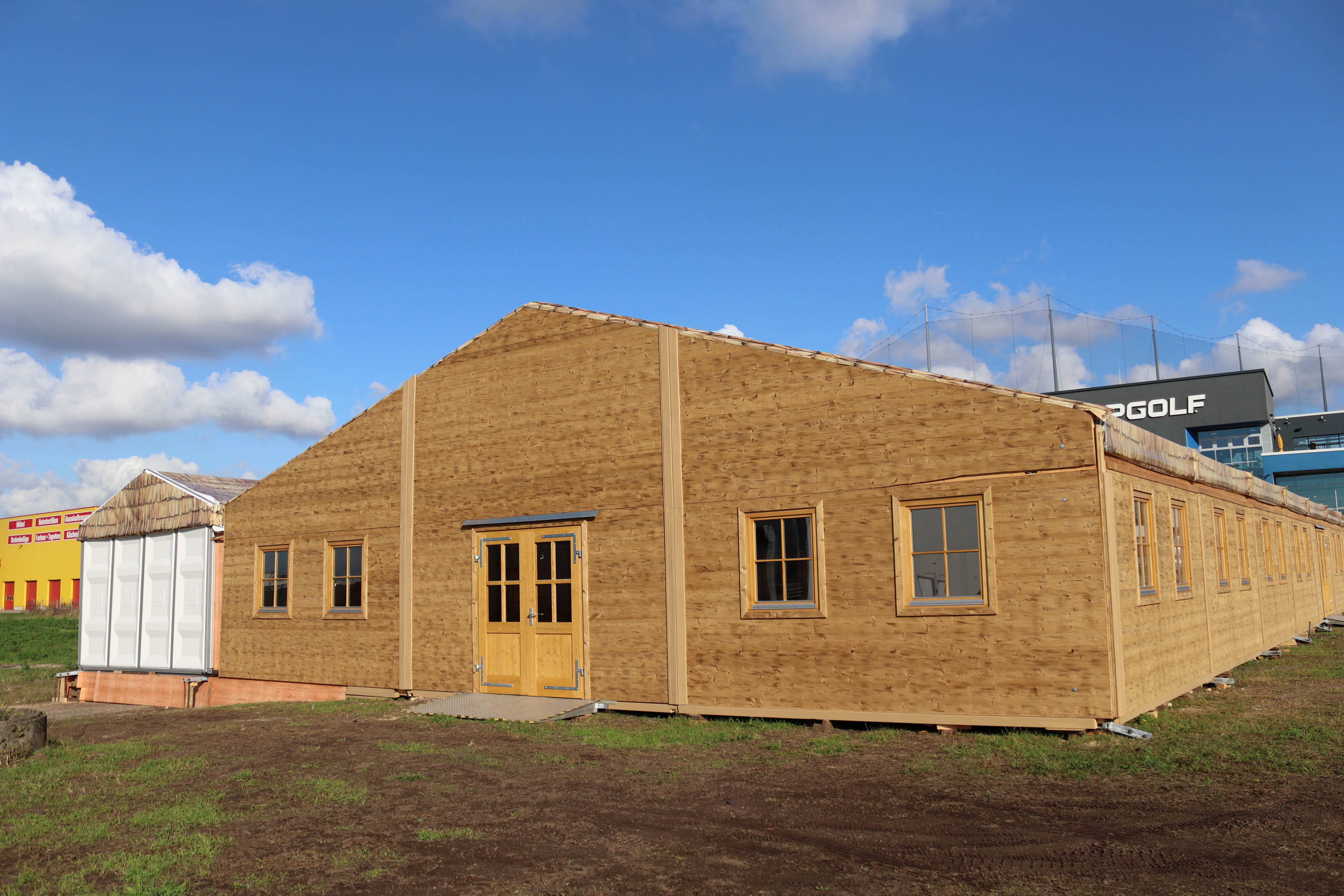 Festzelt im Holz-Design auf einer Wiese unter blauem Himmel