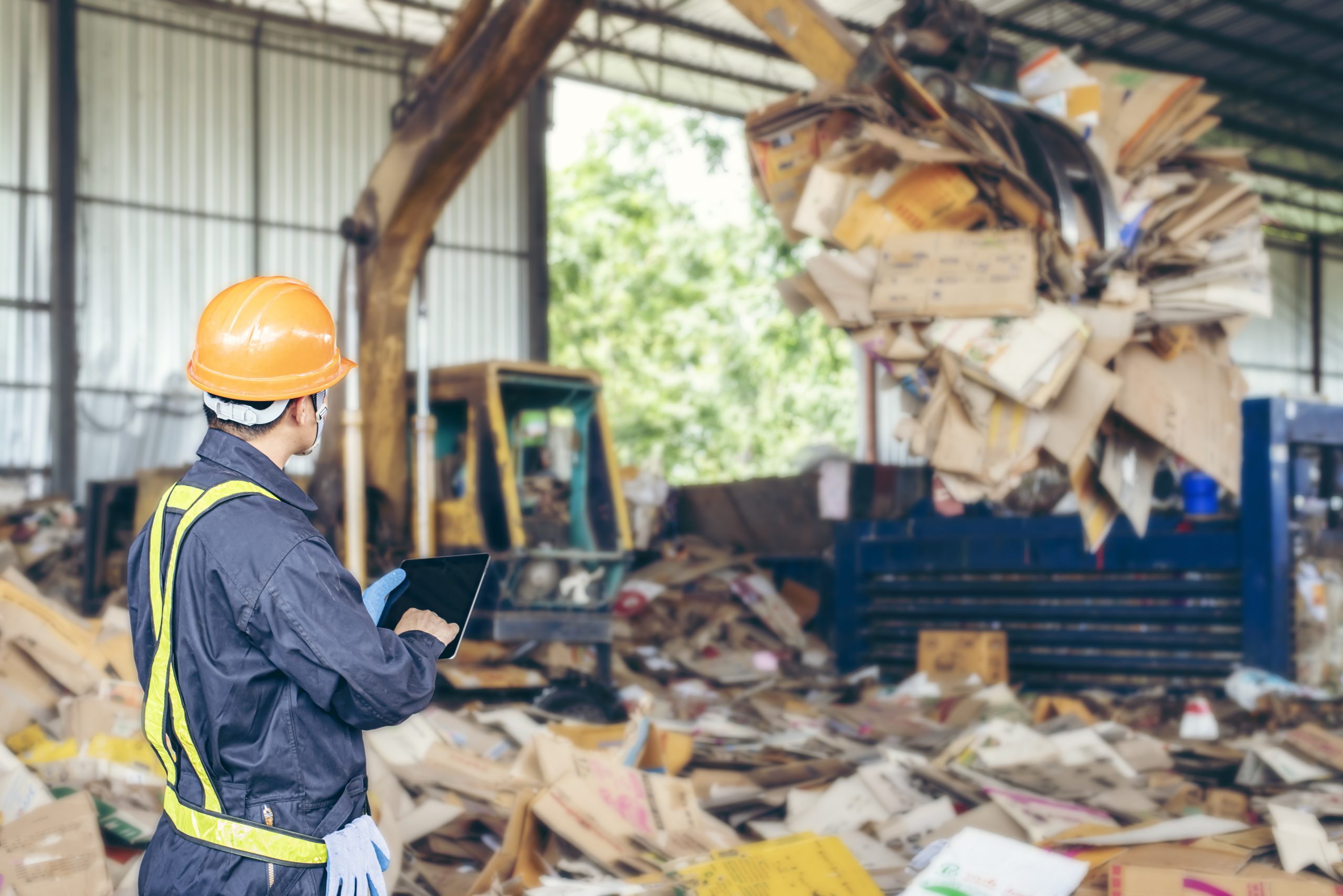 Innenansicht einer Industriehalle für Recycling mit Arbeiter und Kartonpressmaschine