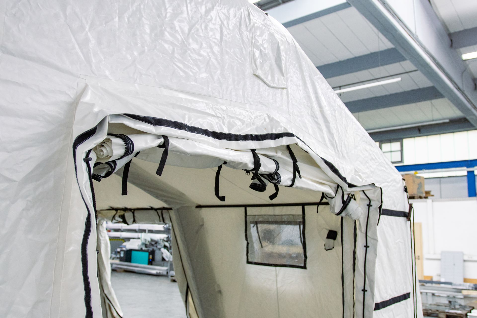 Detailaufnahme des Eingangsbereichs des aufblasbaren Rettungszelts MZI 42 mit eingerolltem Türvorhang und Befestigungsschlaufen